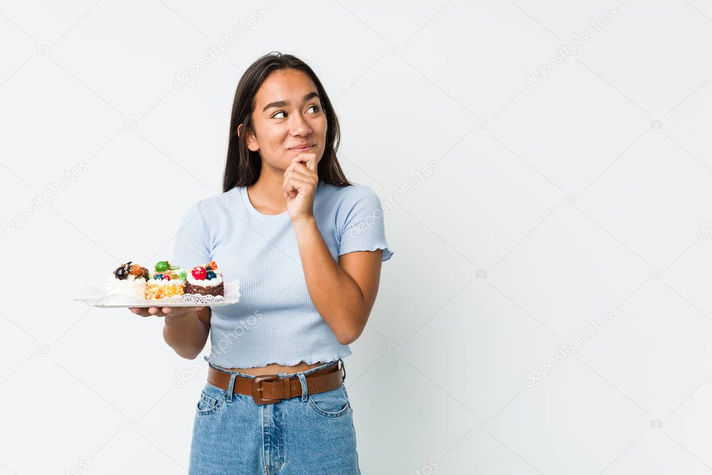 Young mixed race indian holding a sweet cakes looking sideways with doubtful and skeptical expression.