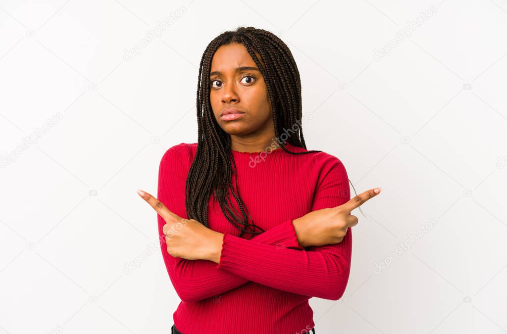 Young african american woman isolated points sideways, is trying to choose between two options.