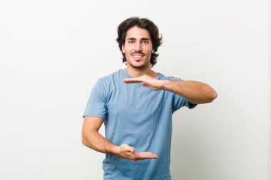 Beyaz arka planda genç yakışıklı bir adam iki eliyle bir şey tutuyor, ürün sunumu..