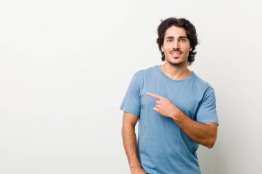 Beyaz bir arkaplanda gülümseyen ve bir kenara işaret eden genç yakışıklı bir adam boş alanda bir şeyler gösteriyor..