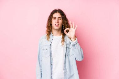 Uzun saçlı adam yalnız poz veriyor bir göz kırpıyor ve elleriyle iyi bir jest yapıyor..