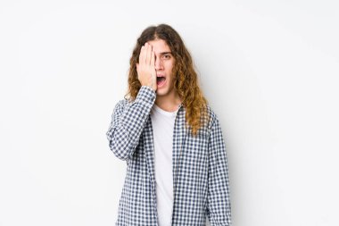 Genç, uzun saçlı adam yalnız poz veriyor. Yüzünün yarısını avuç içiyle kaplayarak eğleniyor..