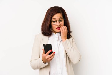 Cep telefonu tutan orta yaşlı Latin bir kadın tırnak yiyor, gergin ve endişeli..