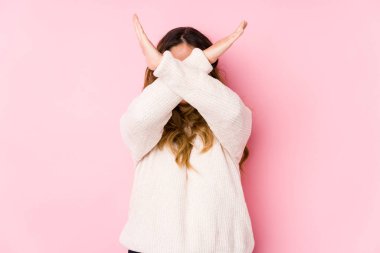 Young curvy woman posing in a pink background isolated keeping two arms crossed, denial concept. clipart