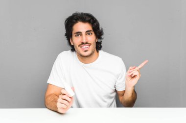 Burun spreyi tutan genç adam işaret parmağıyla işaret ederek gülümsüyor..