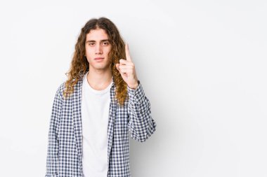 Genç, uzun saçlı adam, yalnız poz veriyor. Bir numarayı parmağıyla gösteriyor..