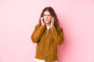 Genç, uzun saçlı adam elleriyle kulaklarını kapatmış poz veriyor..