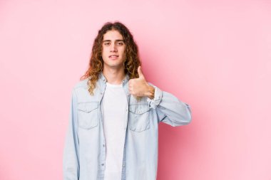 Uzun saçlı adam yalnız poz veriyor, gülümsüyor ve başparmağını kaldırıyor.