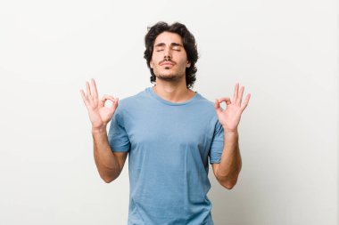 Beyaz arka planda genç ve yakışıklı bir adam sıkı çalışma gününden sonra rahatlıyor. Yoga yapıyor..