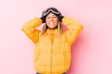 Pembe arka planda kayak kıyafeti giyen beyaz bir kadın ellerini başının üstünde tutarak gülüyor. Mutluluk kavramı.