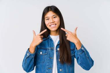 Genç Asyalı kadın gülümsüyor, parmaklarıyla ağzını işaret ediyor..