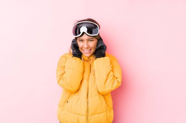 Pembe arka planda kayak kıyafeti giyen beyaz bir kadın kulaklarını elleriyle kapatıyor..