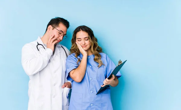 Junges Ärztepaar Posiert Isoliert Vor Blauem Hintergrund Das Gelangweilt Erschöpft — Stockfoto