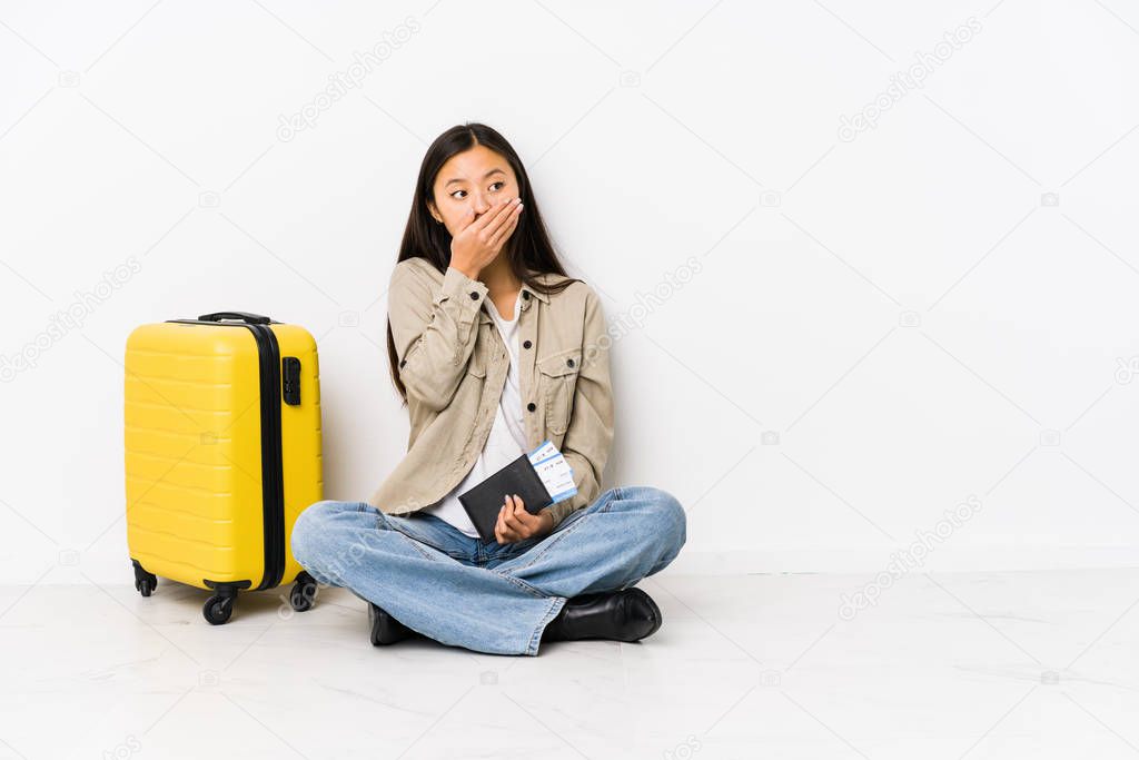 Young chinese traveler woman sitting holding a boarding passes thoughtful looking to a copy space covering mouth with hand.