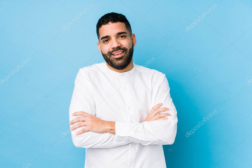 Young latin man against a blue  background isolated who feels confident, crossing arms with determination.