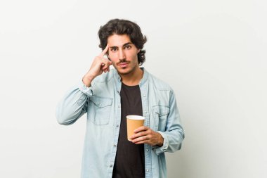 Genç, havalı bir adam kahvesini içiyor. Şakağı parmağıyla işaret ediyor. Düşünüyor, bir işe odaklanıyor..