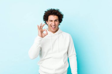 Mavi arka planda genç bir sporcu bir gözünü kırpar ve elleriyle iyi bir jest yapar..