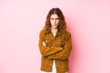 Genç, uzun saçlı, soyutlanmış, hoşnutsuzca kaşlarını çatan, kollarını kavuşturan bir adam..
