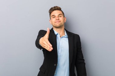 Genç, yakışıklı, beyaz bir adam kameraya elini uzatıp selam veriyor..