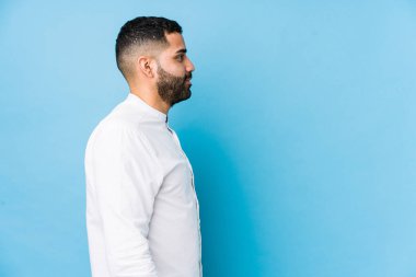 Mavi arka planda genç bir latin adam, yanlamasına soldan bakıyor..