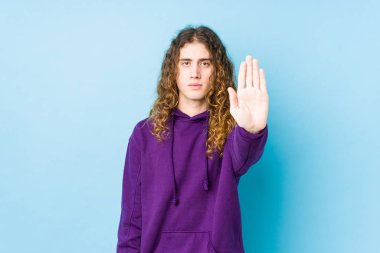 Uzun saçlı adam yalnız poz veriyor. Elini uzatıp dur işareti gösteriyor. Bu da seni engelliyor..