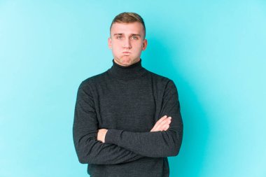 Mavi arka plandaki genç beyaz adam yanakları siliyor, yorgun bir ifadesi var. Yüz ifadesi kavramı.