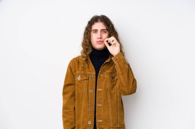 Uzun saçlı adam, izole bir şekilde poz veriyor. Parmakları dudaklarında, sır saklıyor..