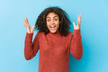 Genç Afro-Amerikan kıvırcık saçlı kadın hoş bir sürpriz yaşıyor, heyecanlı ve el kaldırıyor..