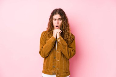 Uzun saçlı genç adam yalnız poz veriyor şans için dua ediyor, şaşırmış ve ağzını açıp önüne bakıyor..