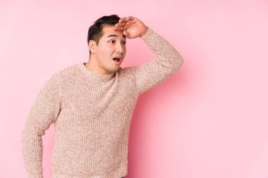 Pembe arka planda poz veren kıvrımlı genç adam çok uzaklara bakıyor ve elini alnına koyuyor..