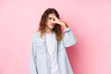 Uzun saçlı adam kameraya parmaklarıyla göz kırpıyor, utangaç bir şekilde yüzünü kapatıyor..