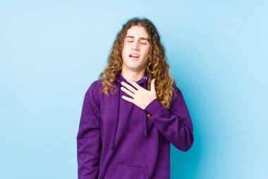 Uzun saçlı adam yalnız poz veriyor. Kahkahalar atıyor. Elini göğsüne koyuyor..