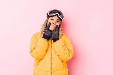 Young caucasian woman wearing a ski clothes in a pink background doubting between two options.