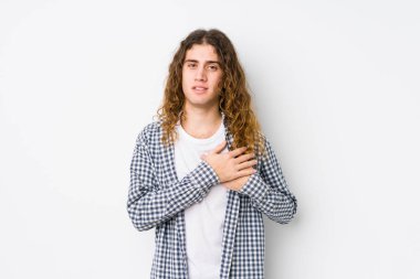 Yalnız poz veren uzun saçlı genç adam, avuçlarını göğsüne bastıran dostça bir ifadeye sahiptir. Aşk konsepti.