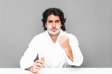 Sakalını kesen genç bir adam kameraya yumruğunu gösteriyor, agresif bir yüz ifadesi..