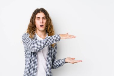 Genç, uzun saçlı, yalnız poz veren, şok olmuş ve hayrete düşmüş bir adam. Ellerinin arasında bir kopya alanı tutuyor..