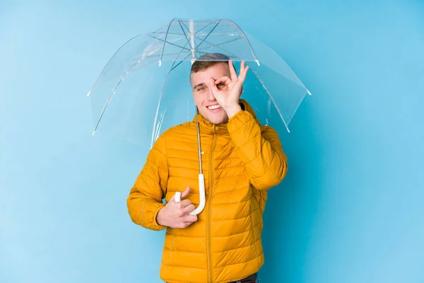 年轻的高加索人拿着一把伞兴奋地保持着对着眼睛的正常姿势 — 图库照片