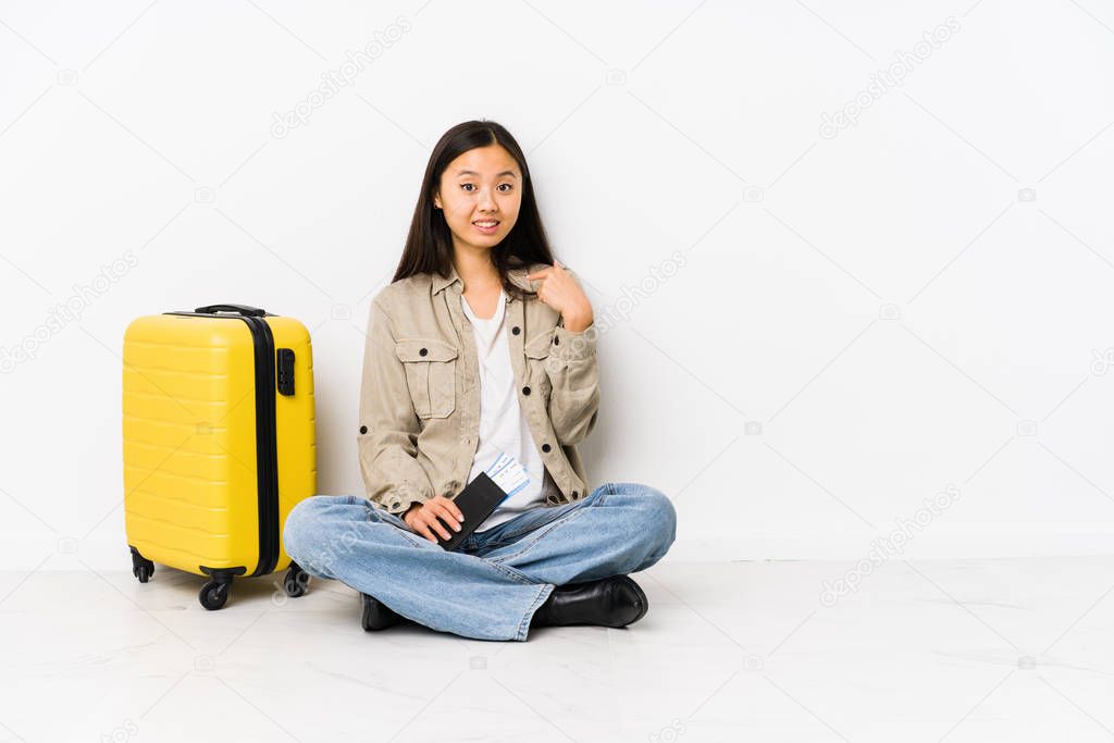 Young chinese traveler woman sitting holding a boarding passes person pointing by hand to a shirt copy space, proud and confident