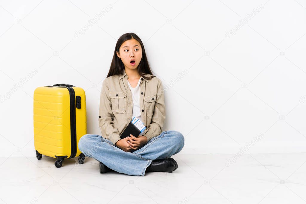 Young chinese traveler woman sitting holding a boarding passes being shocked because of something she has seen.