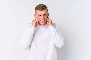 Beyaz arka planda genç beyaz bir adam kulaklarını elleriyle kapatıyor..