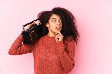 Young afro woman holding a cassete isolated looking sideways with doubtful and skeptical expression.