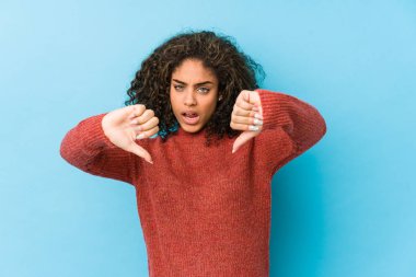 Genç Afro-Amerikalı kıvırcık saçlı kadın baş parmağını aşağı gösteriyor ve hoşlanmadığını ifade ediyor..