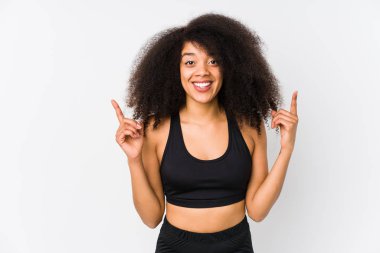 Young african american sporty woman indicates with both fore fingers up showing a blank space.