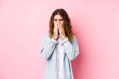 Uzun saçlı adam yalnız poz veriyor. Bir şeye gülüyor, elleriyle ağzını kapatıyor..