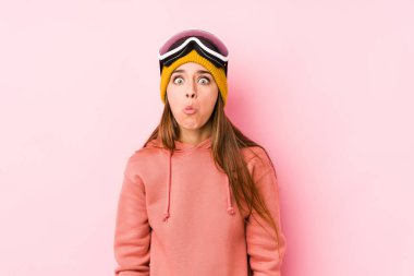 Young caucasian woman wearing a ski clothes isolated shrugs shoulders and open eyes confused. clipart