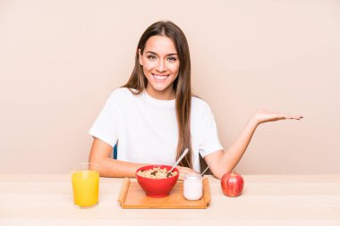 Genç, beyaz bir kadın kahvaltısını yalnız yapıyor. Bir avuç içinde fotokopi odası ve belinde başka bir el tutuyor..