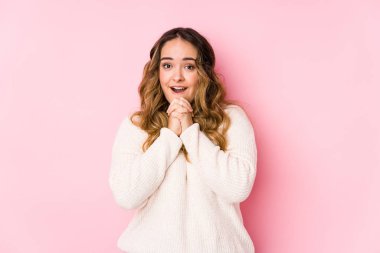 Pembe arka planda poz veren kıvrımlı genç bir kadın yalnız başına şans diliyor, şaşırıyor ve önüne bakıyor..