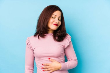 Orta yaşlı Latin kadın karnına dokunuyor, nazikçe gülümsüyor, yemek yiyor ve tatmin oluyor..