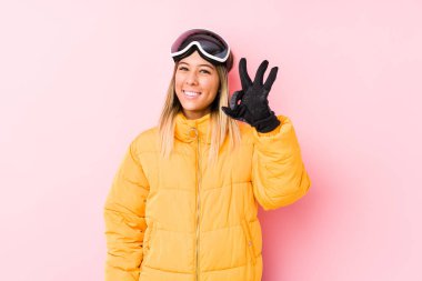 Pembe arka planda kayak kıyafeti giyen beyaz bir kadın. Neşeli ve kendinden emin..