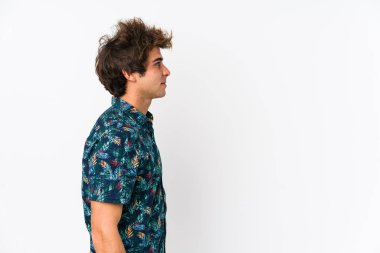 Genç beyaz bir adam çiçek tişörtü giyiyor, yanlamasına sola bakıyor, poz veriyor..